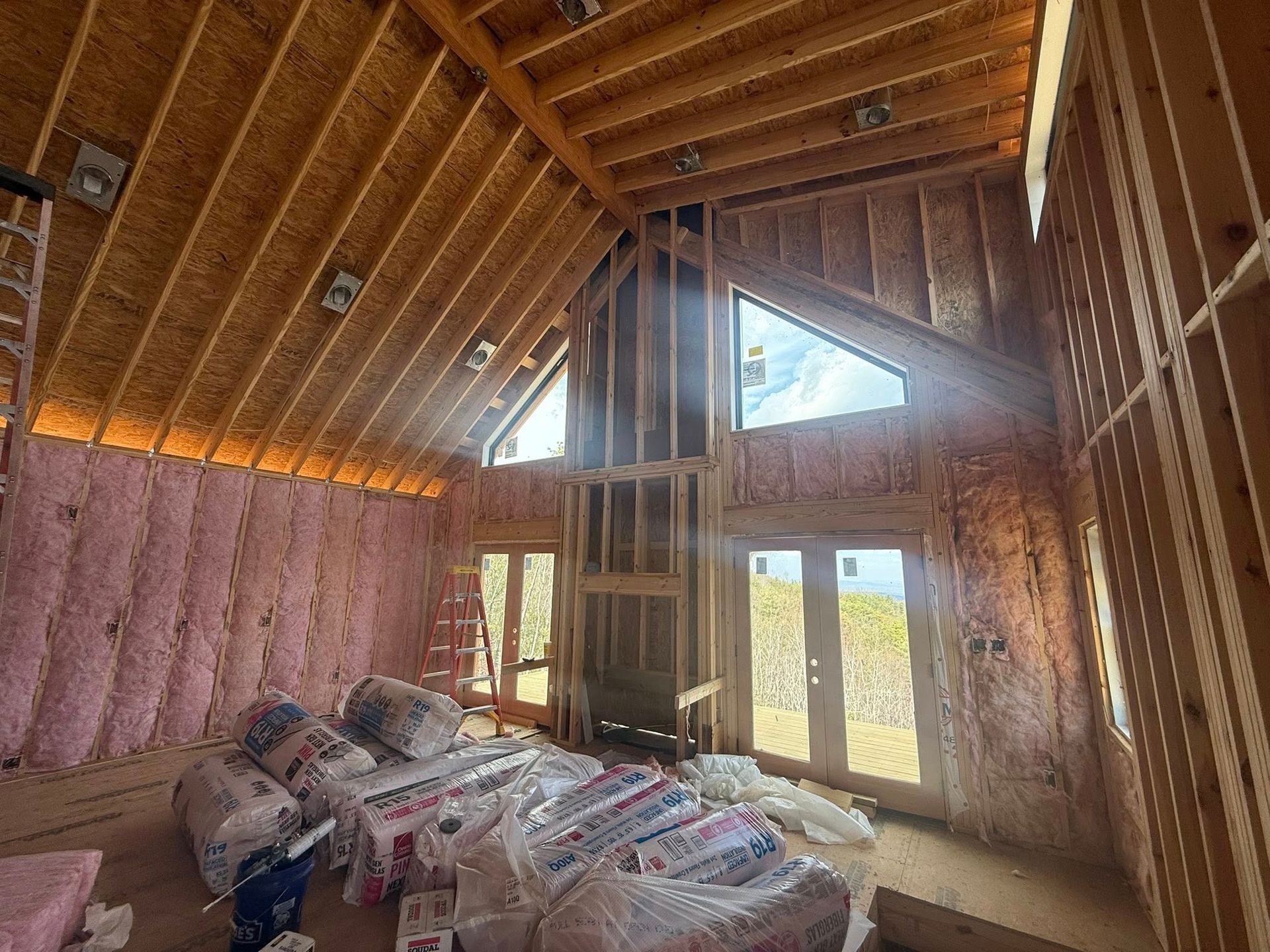 Unfinished attic room with exposed wood framing, insulation, and stacked construction materials by a window.