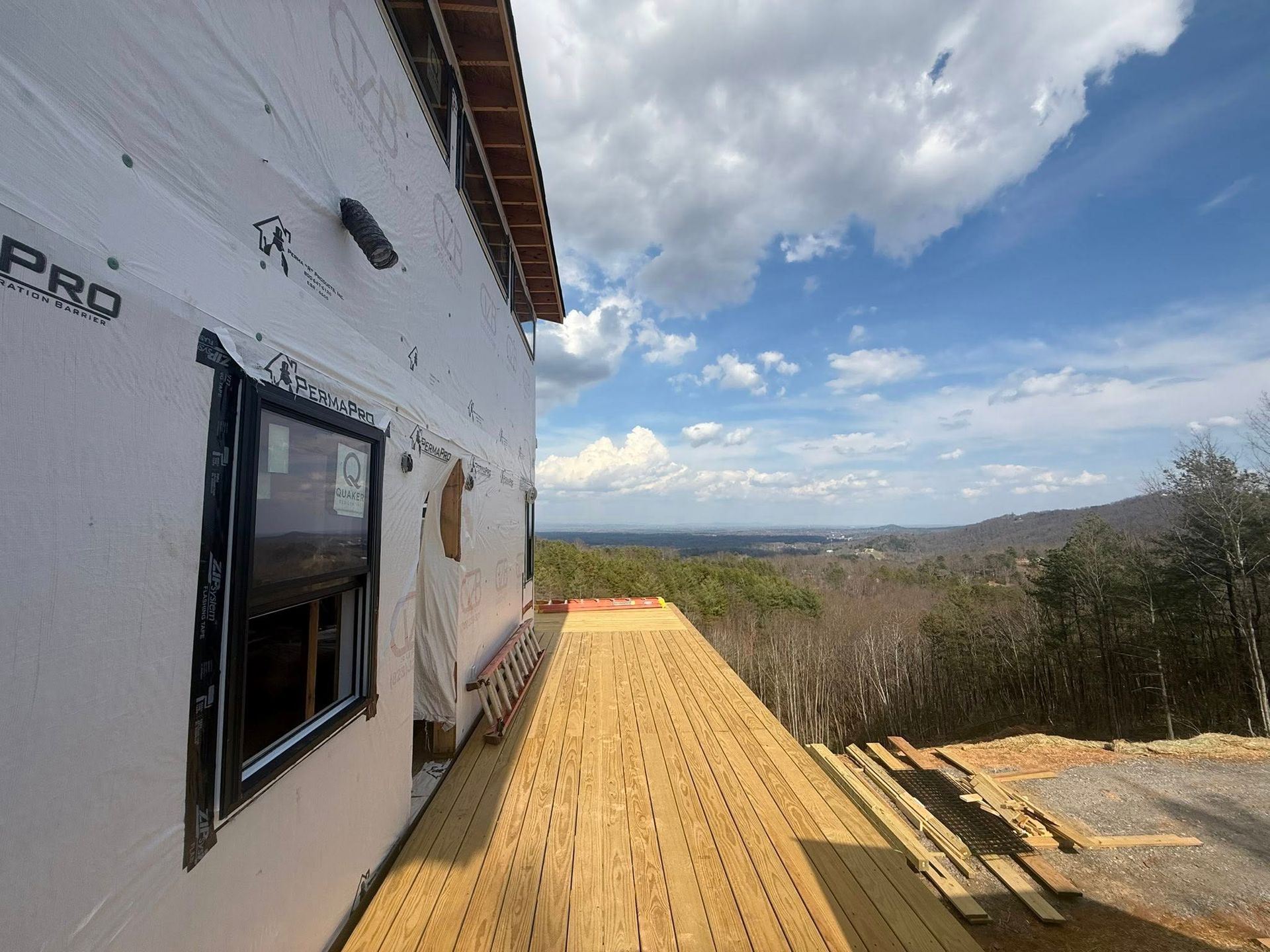 Wooden deck beside a house under construction, overlooking a wooded valley under a cloudy sky