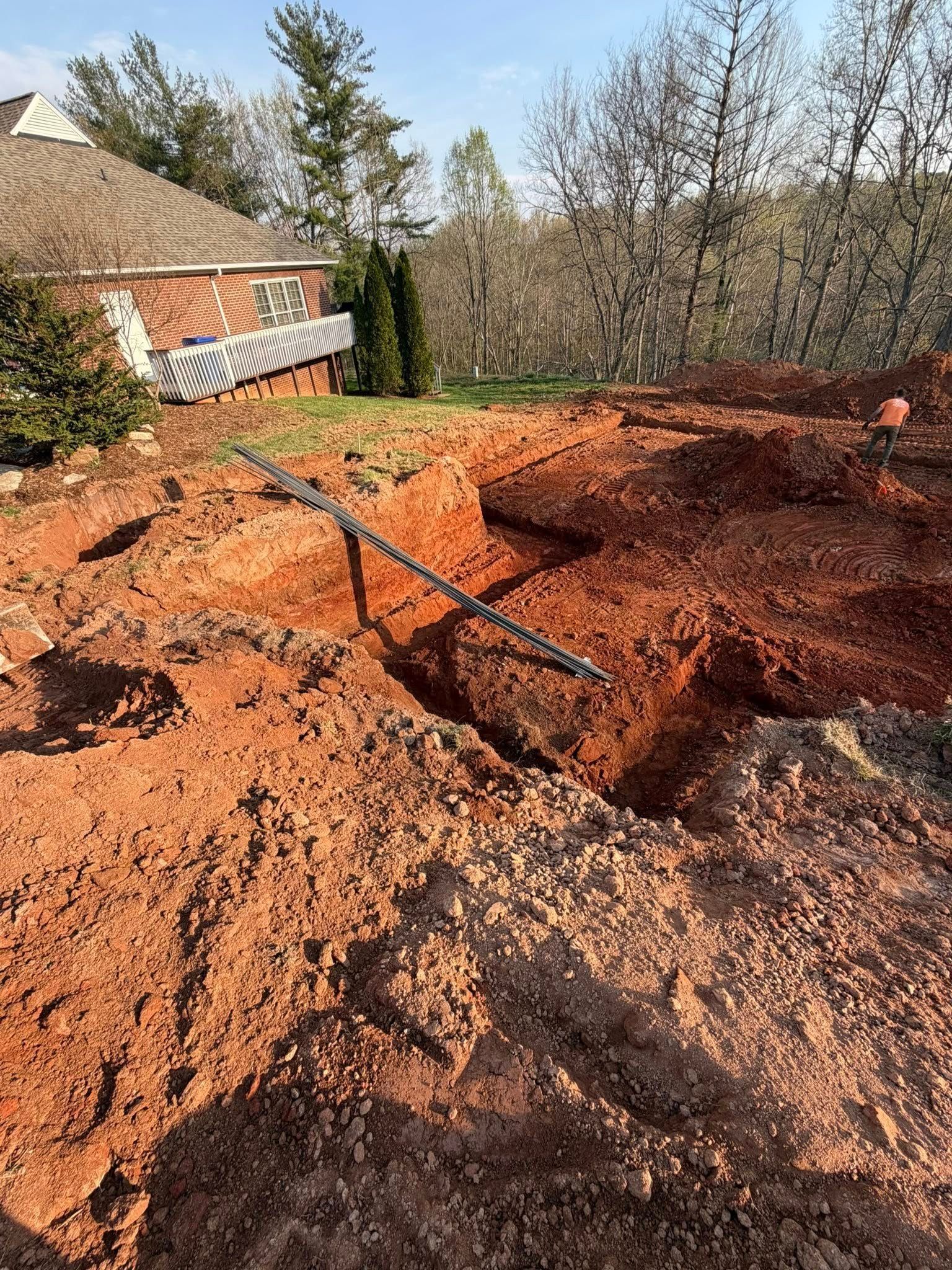 Large dug-up red clay yard with trenches and a house in the background under clear daylight