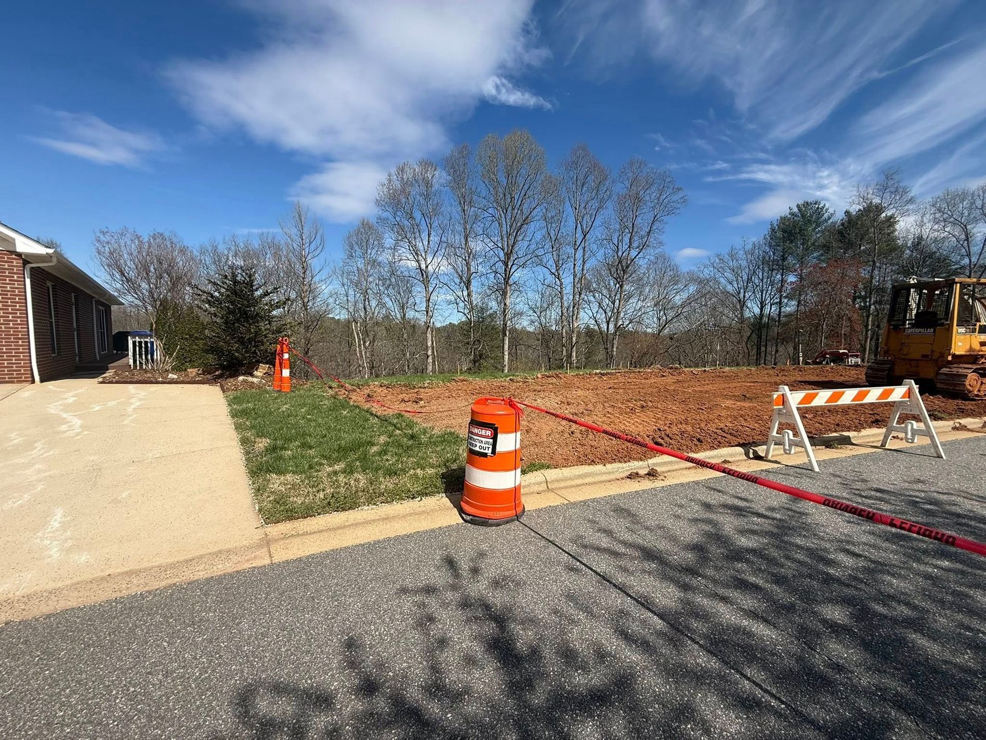 Road construction area with orange barrels, barricade, and sand pile beside a building under a blue sky