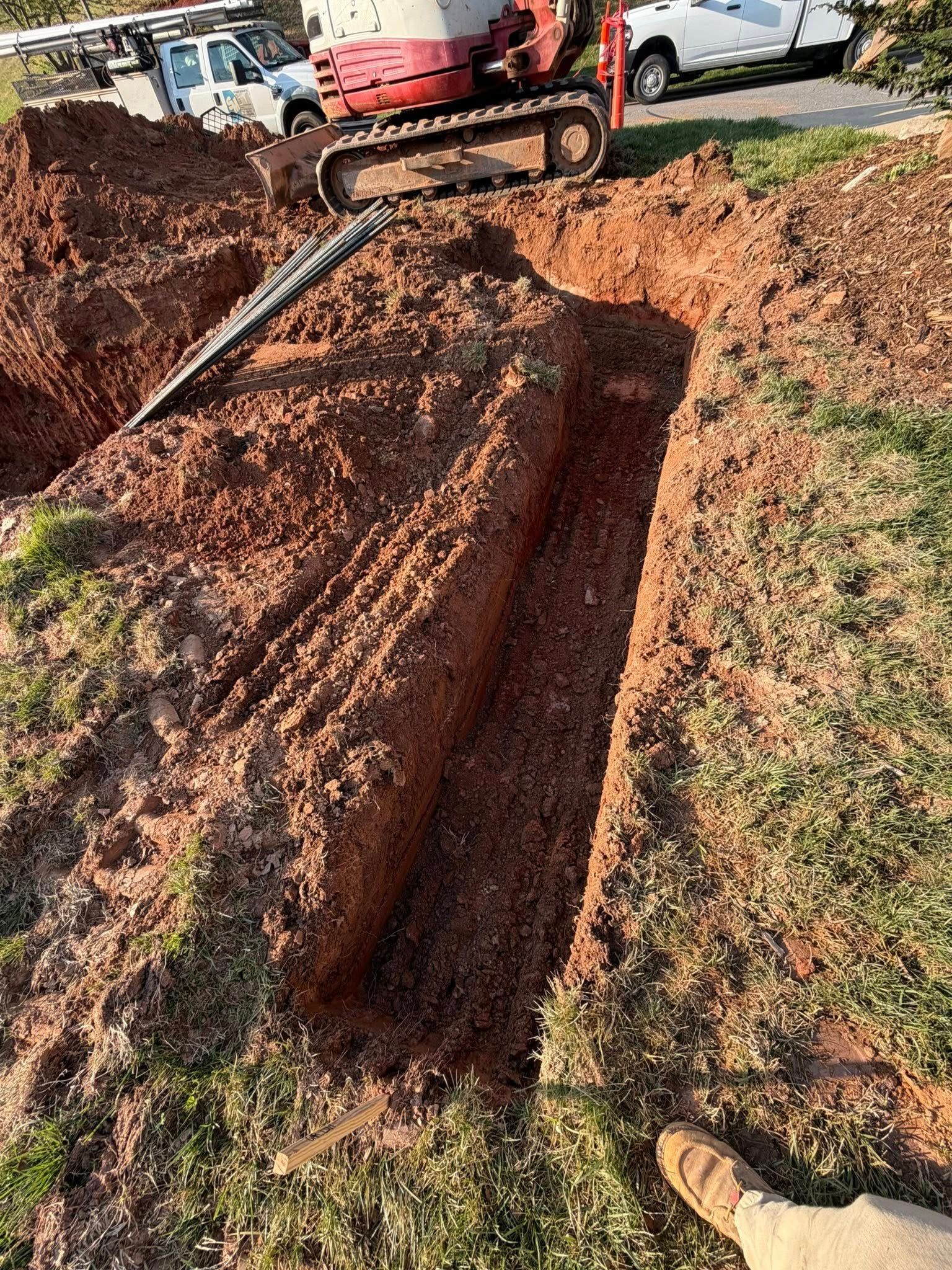 Mini excavator digging a long trench through a leaf-covered yard beside a driveway
