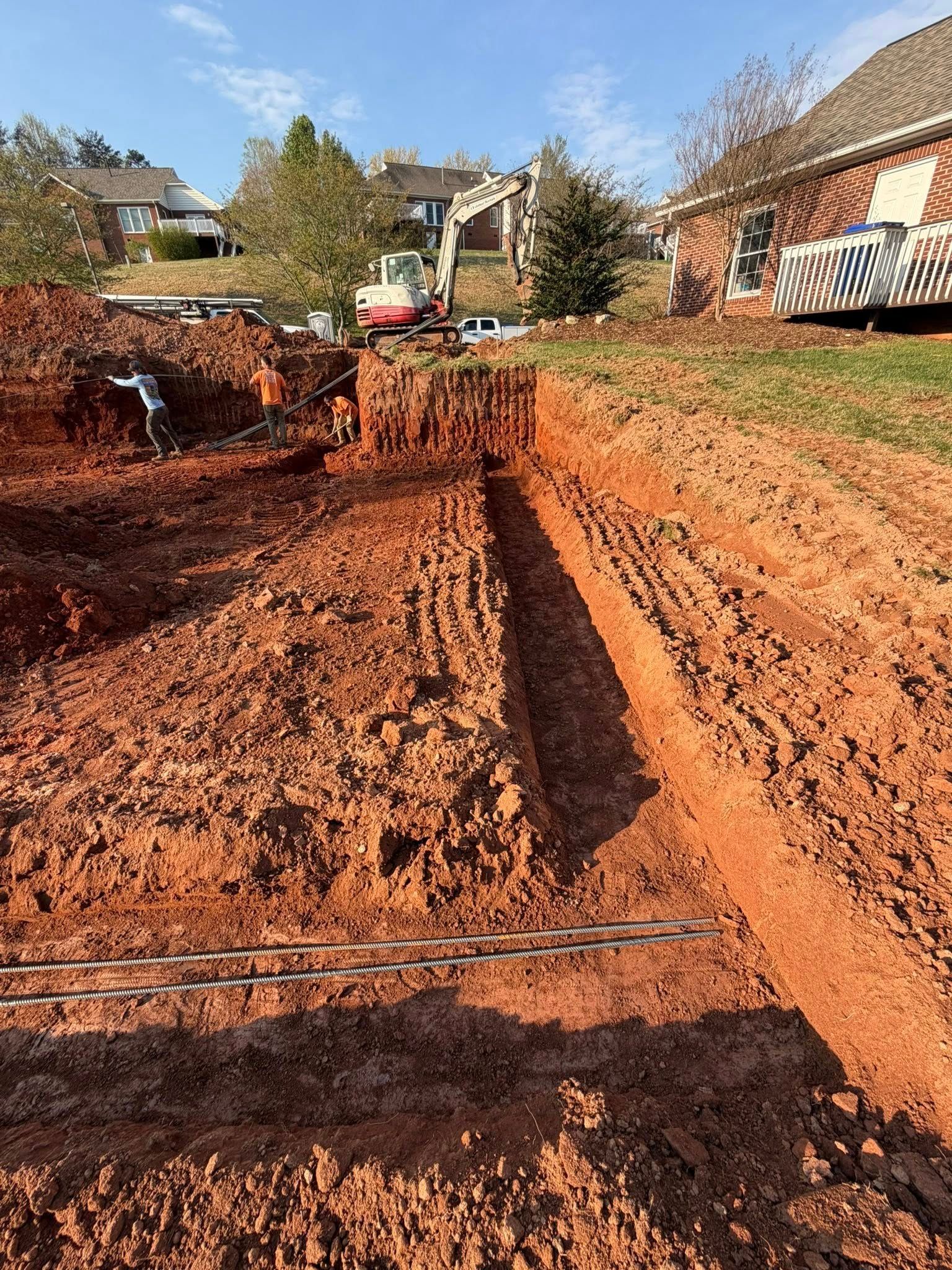 Freshly dug red clay trench in a residential neighborhood with houses and trees in the background