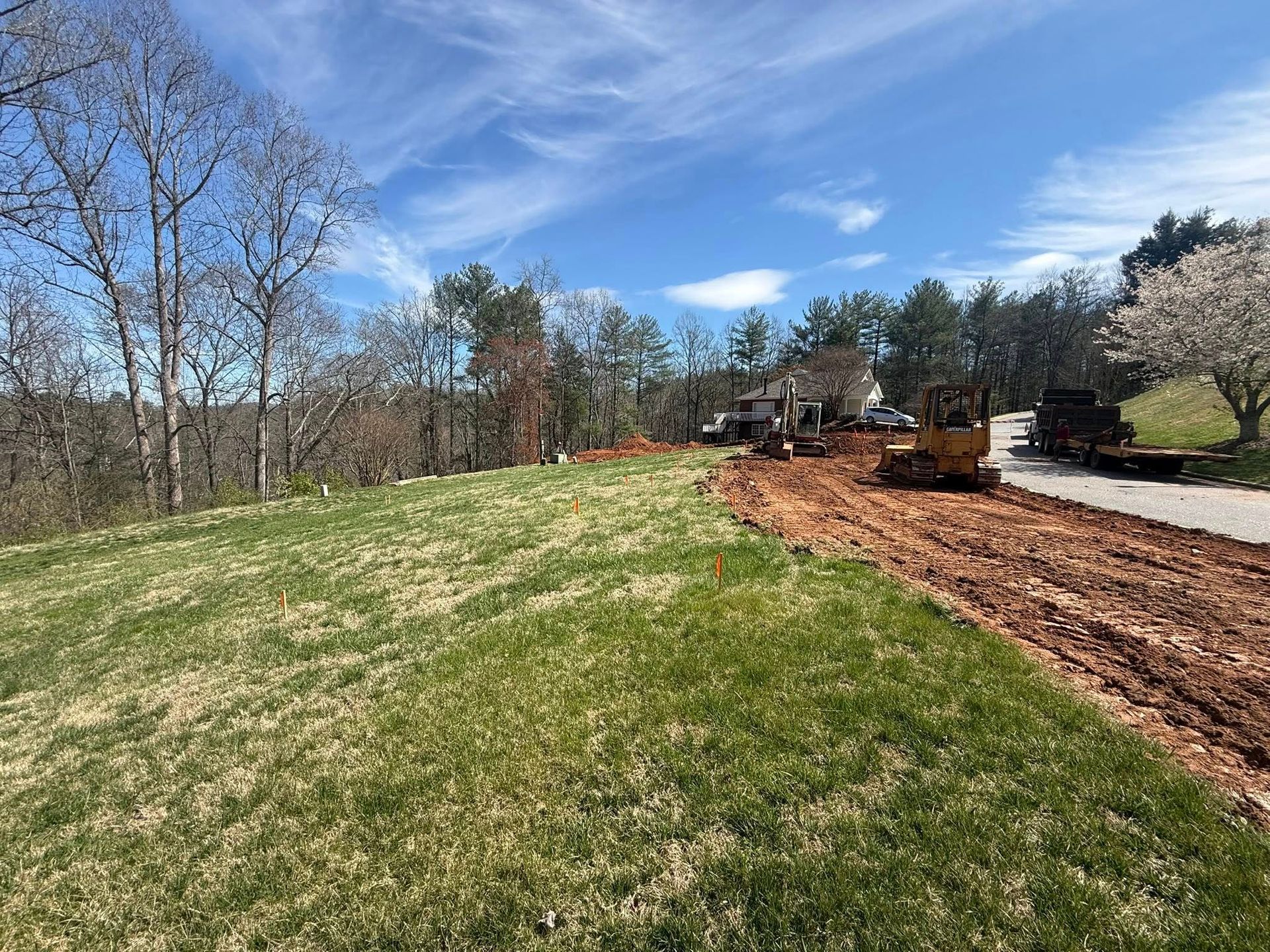Partially cleared hillside beside a road, with a bulldozer and dirt work under a blue sky