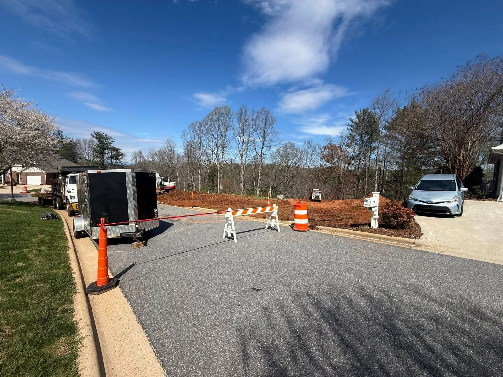 Roadwork area with orange cones, barricades, and a white van on a gravel roadside under a blue sky