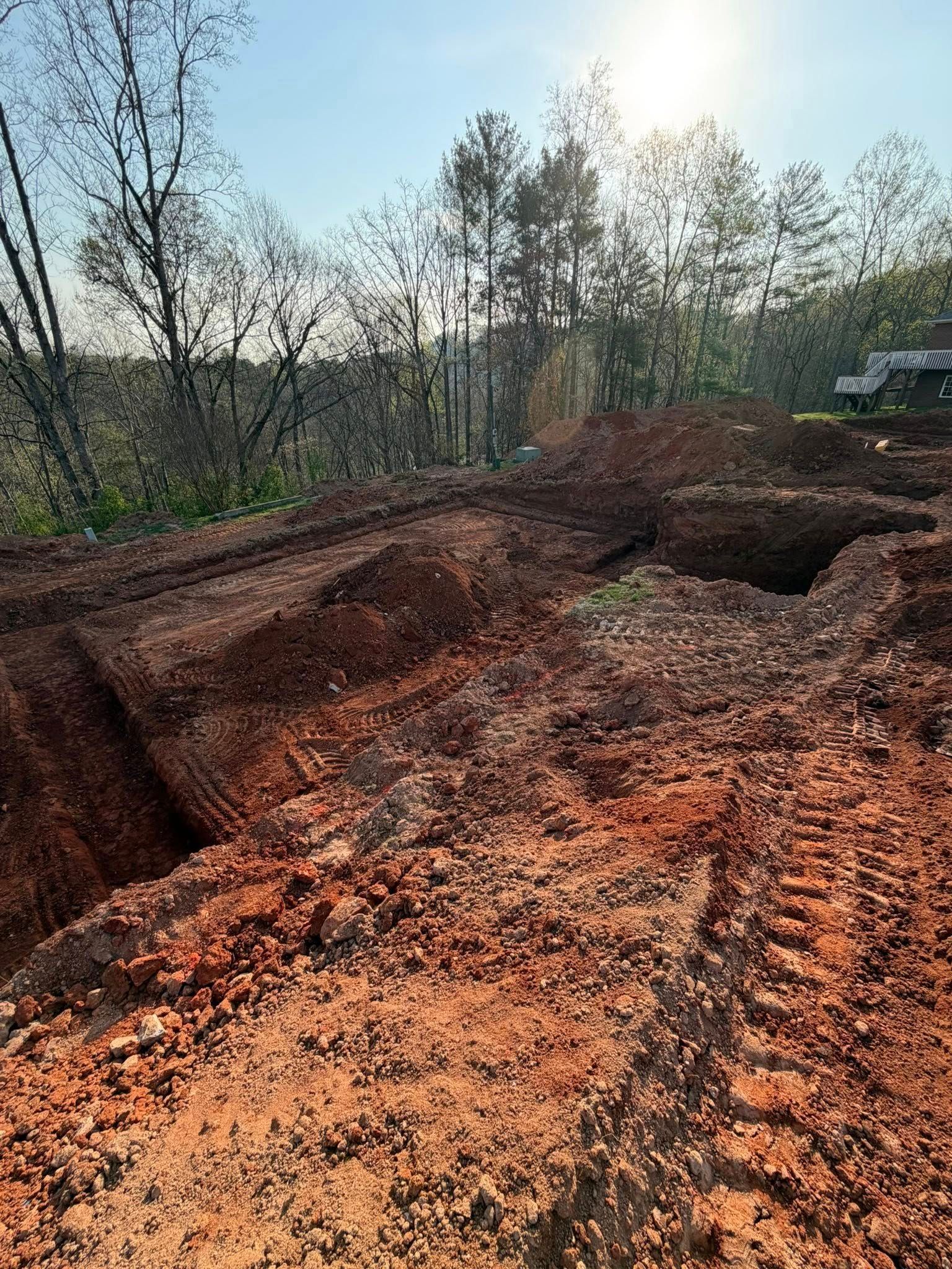 Freshly dug red clay trench along a wooded dirt road in sunlight