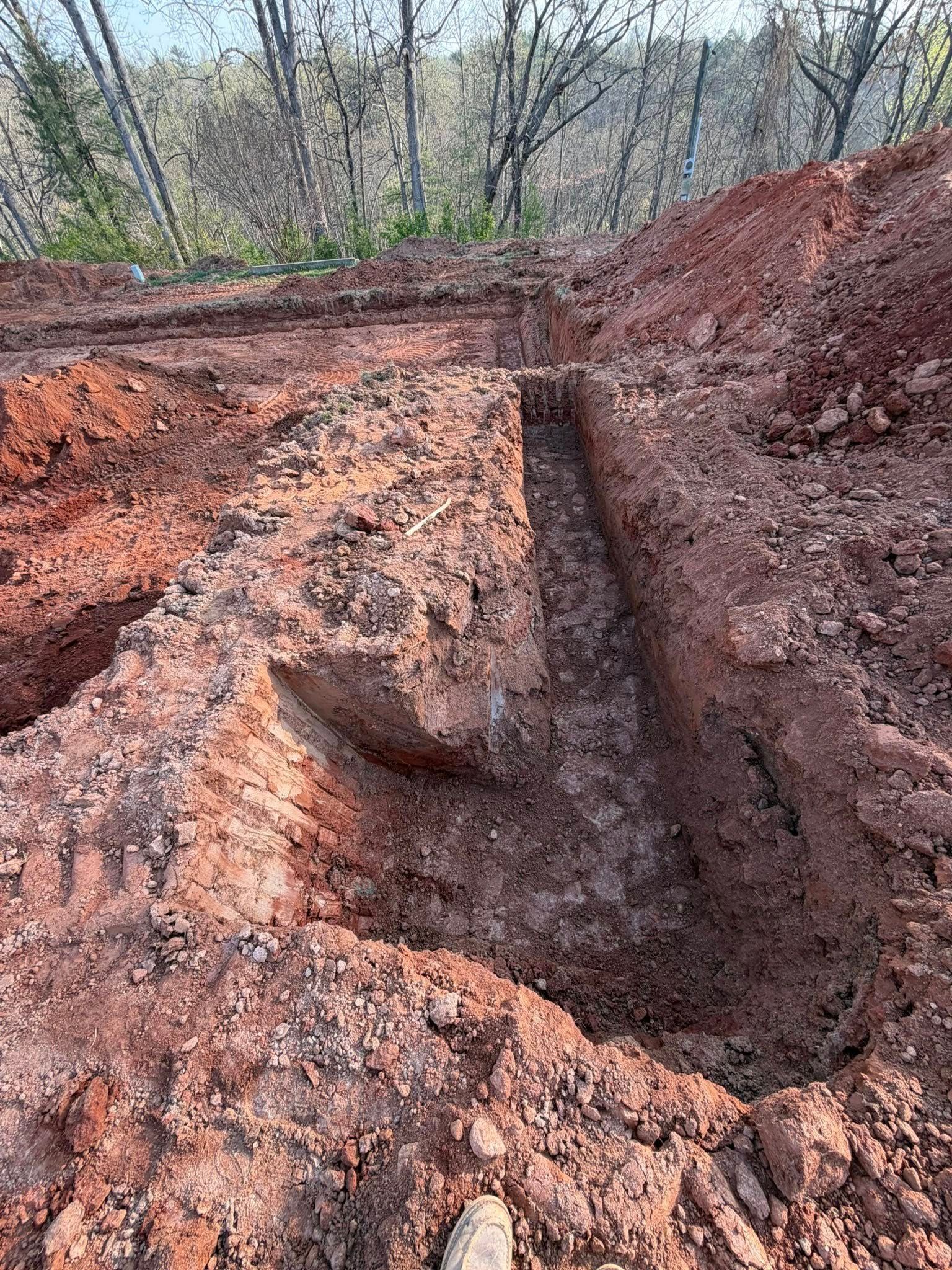 Freshly dug red clay trench with an eroded dirt embankment in a wooded area