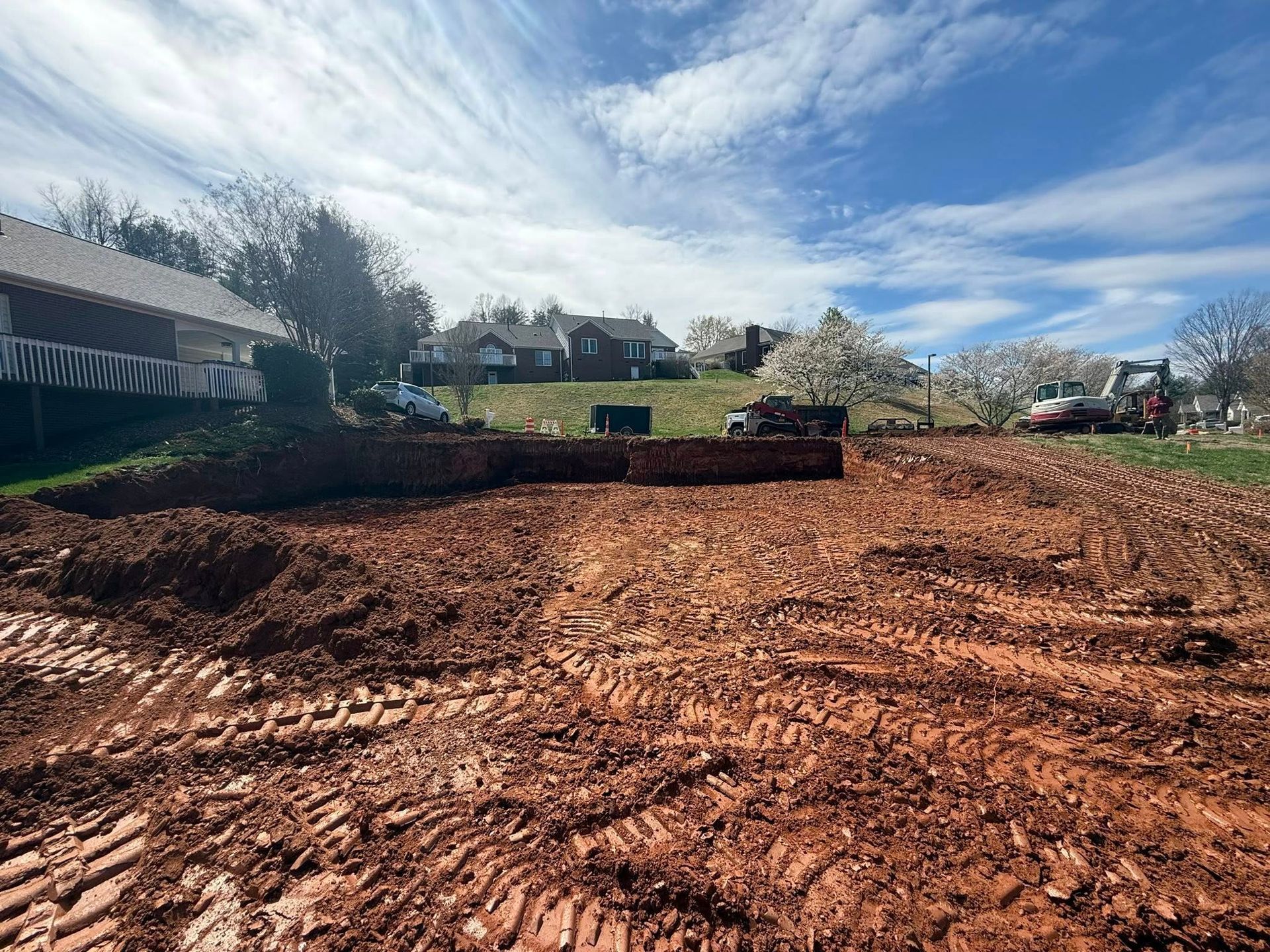 Cleared dirt lot with a small bulldozer under a blue sky, houses and trees in the background