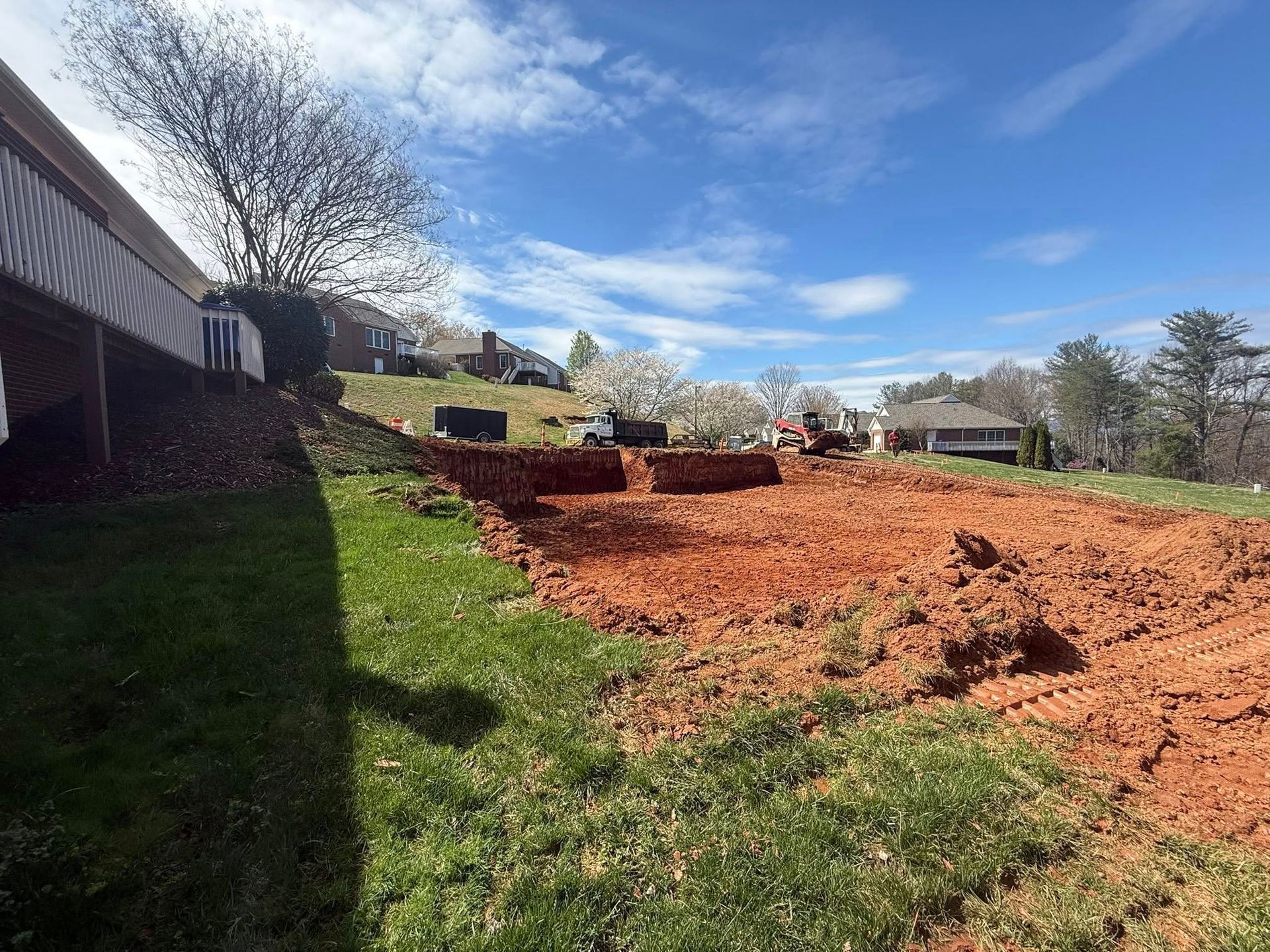 Dirt-cleared backyard with a grassy edge, tree stumps, and houses under a blue sky