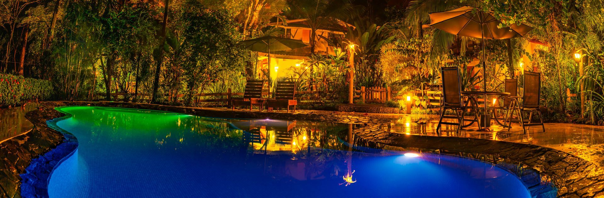A large swimming pool is lit up at night with colorful lights.