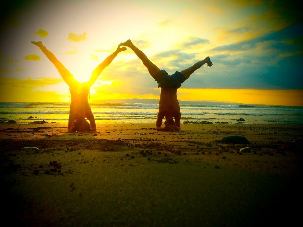 Two people are doing handstands on the beach at sunset