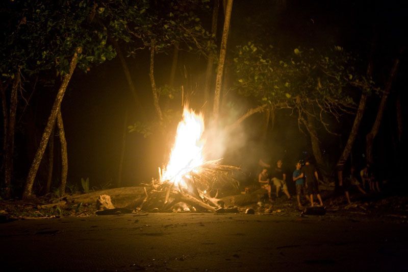 A group of people are standing around a fire in the woods at night.
