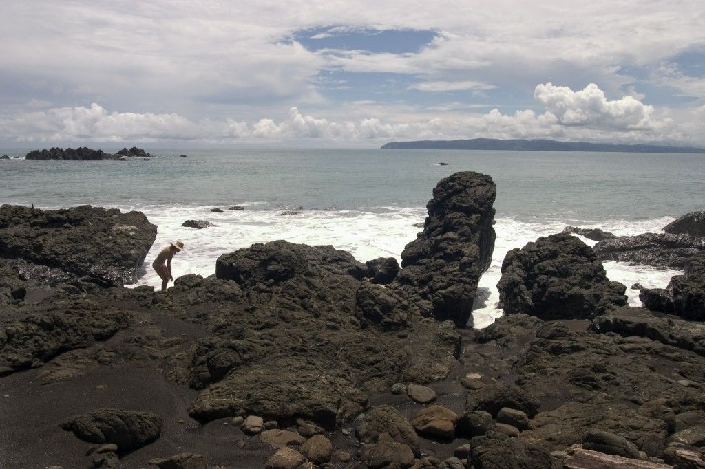 A person is standing on a rocky beach near the ocean.