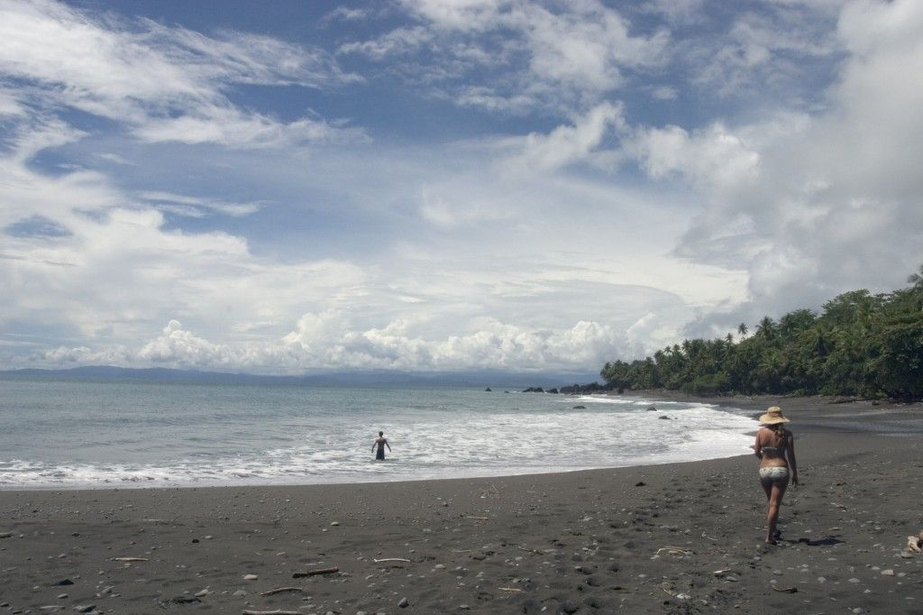 A woman is walking on a black sandy beach near the ocean.