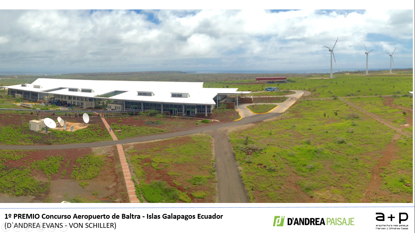 Una vista aérea de un gran edificio en un campo con molinos de viento al fondo.