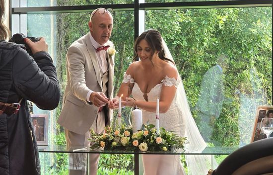 A bride and groom kissing during their wedding ceremony while a man stands at a podium.