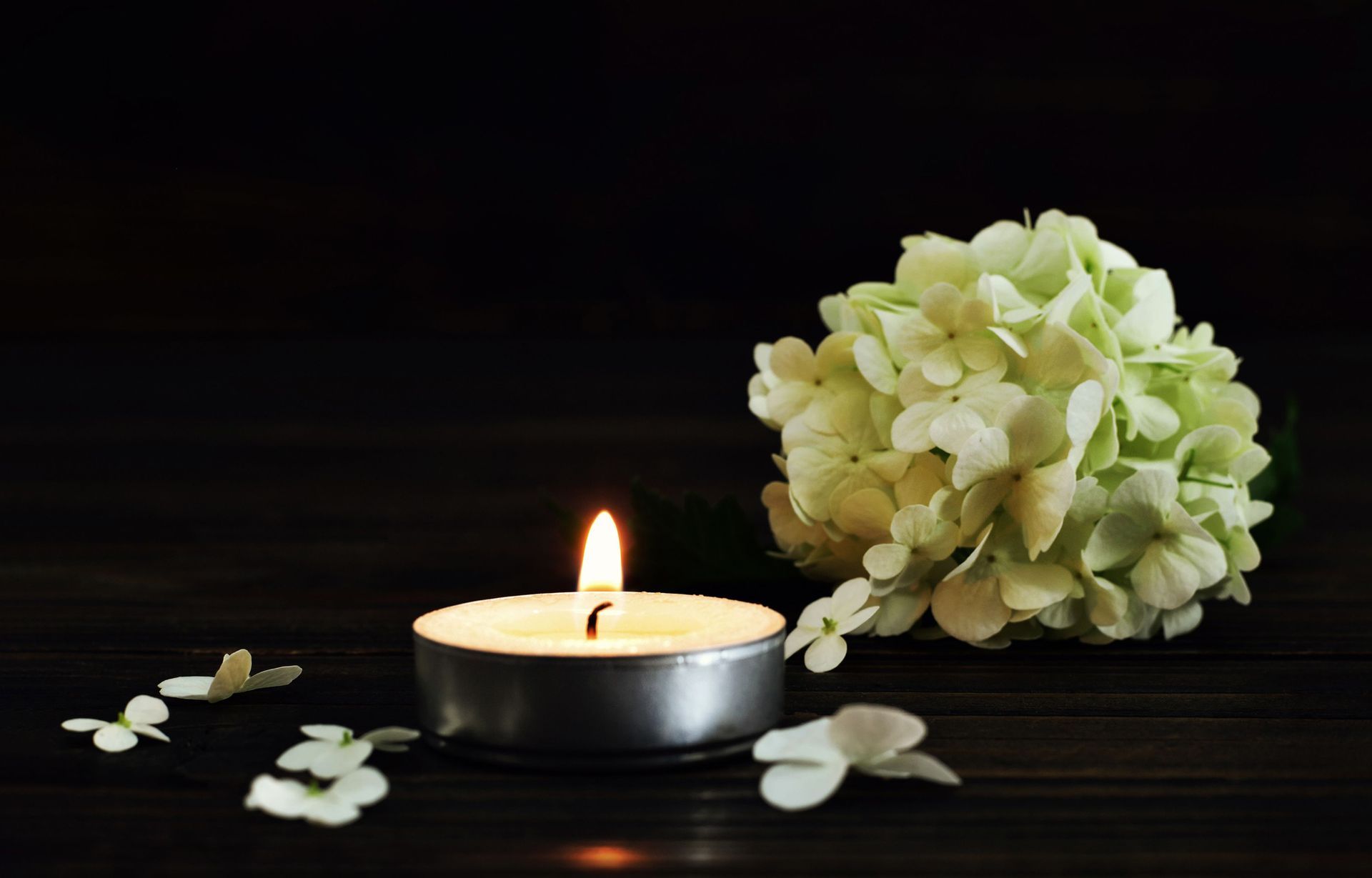 A lit candle and flowers on a wooden table.