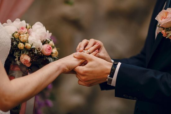 A bride and groom are getting married and the groom is putting a wedding ring on the bride 's finger.
