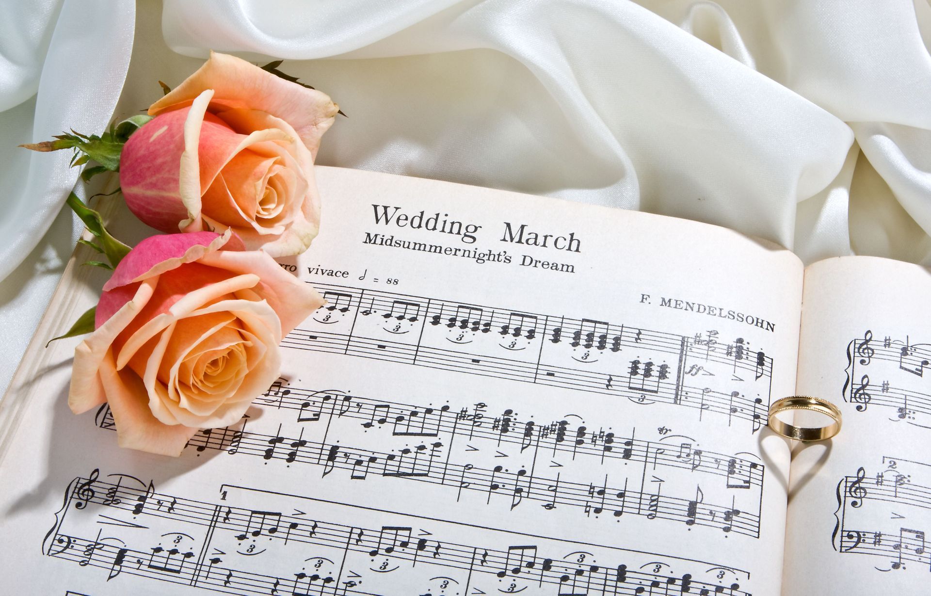 Two roses sit on top of an open music book that says wedding march