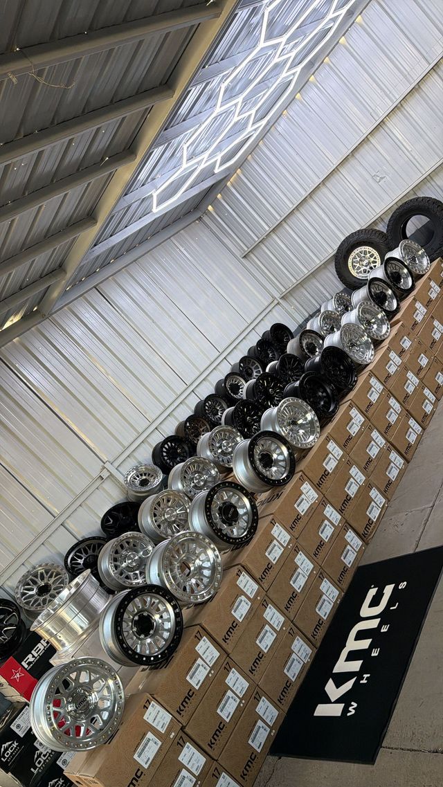 Four black alloy car wheels arranged on a light floor against a white wall.