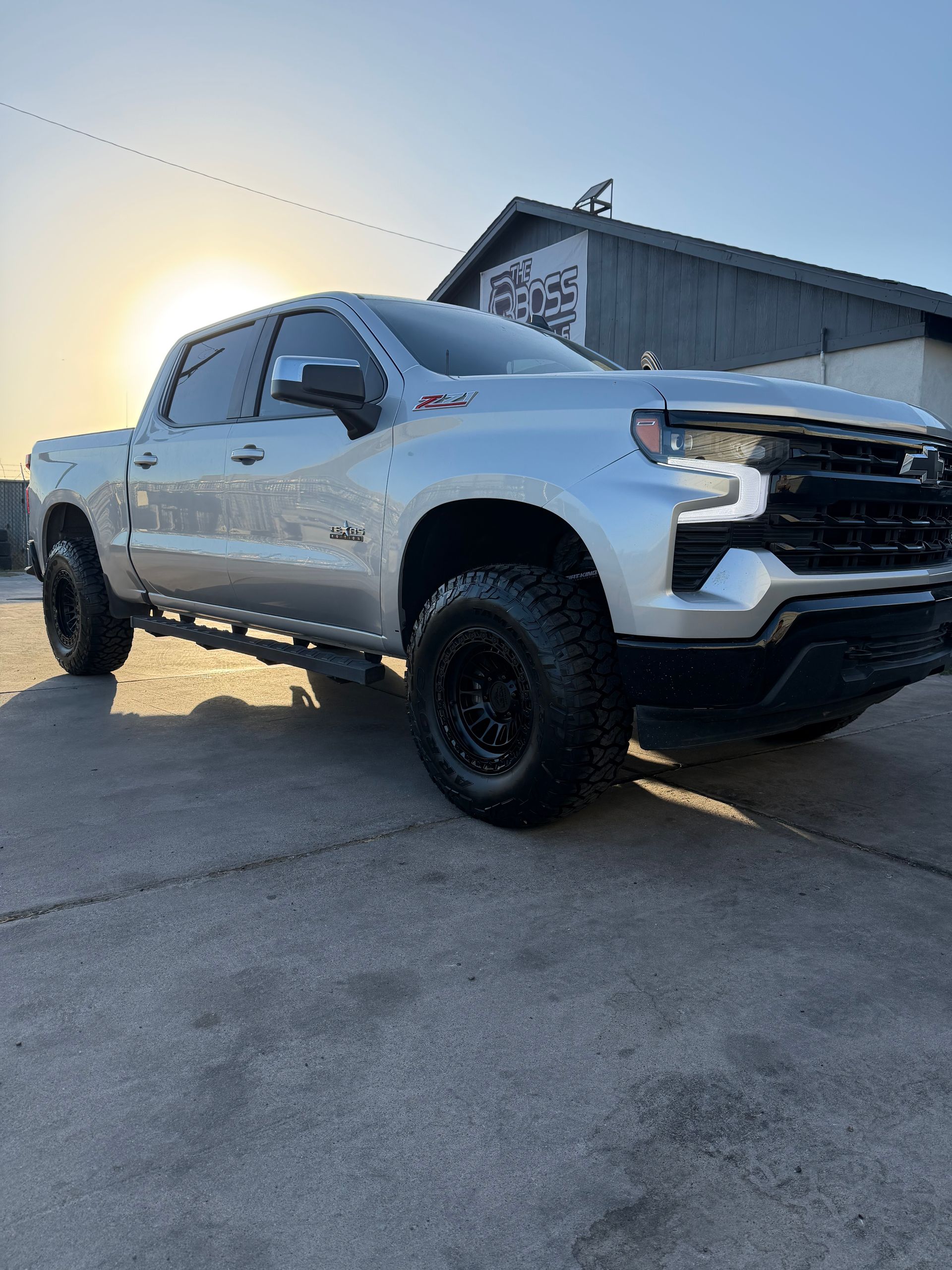 White lifted pickup truck parked on a driveway beside a building at sunset