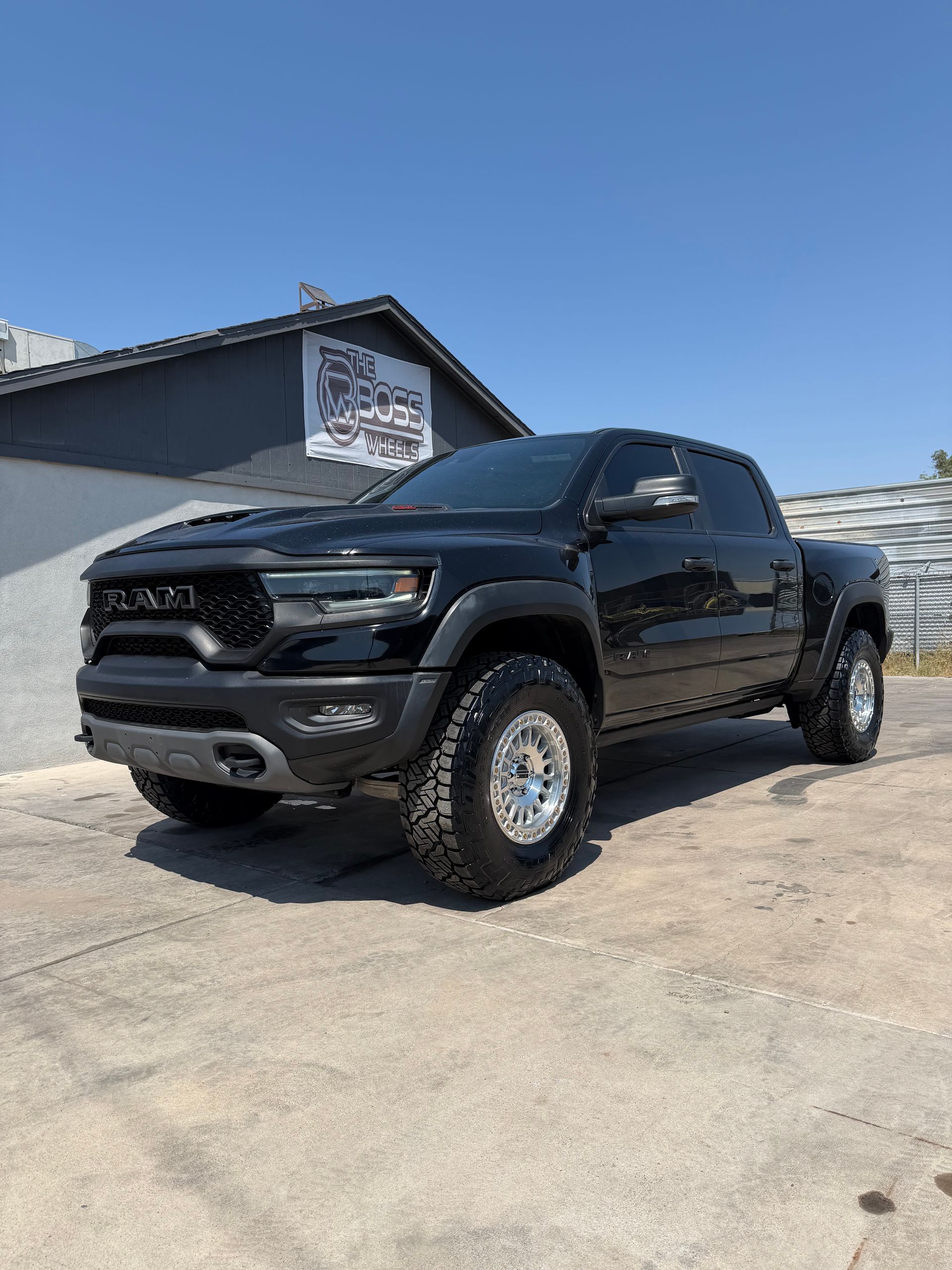 Black pickup truck parked on a sunny lot beside a building under a clear blue sky