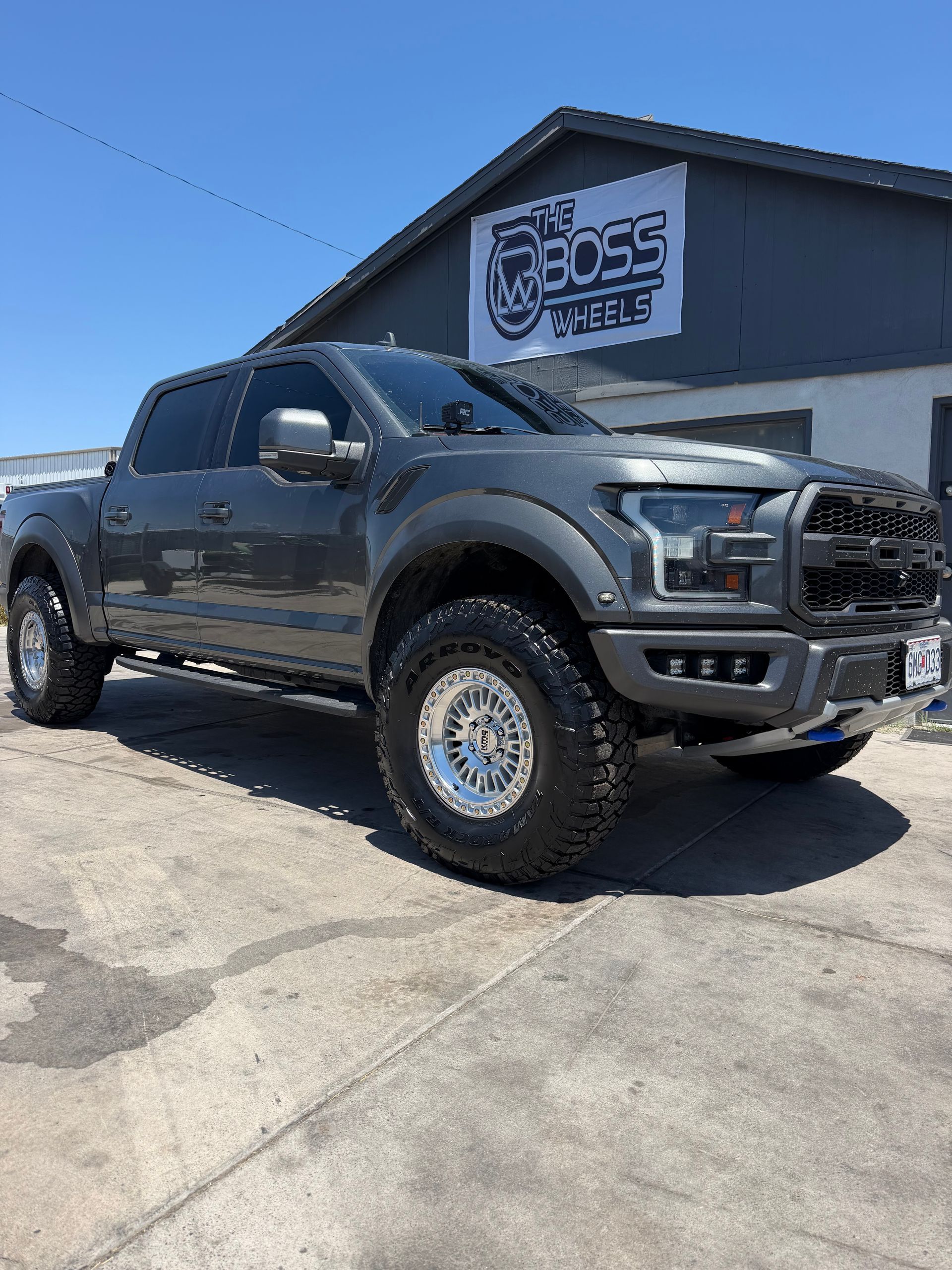 Dark gray lifted pickup truck parked outside a shop on a sunny day
