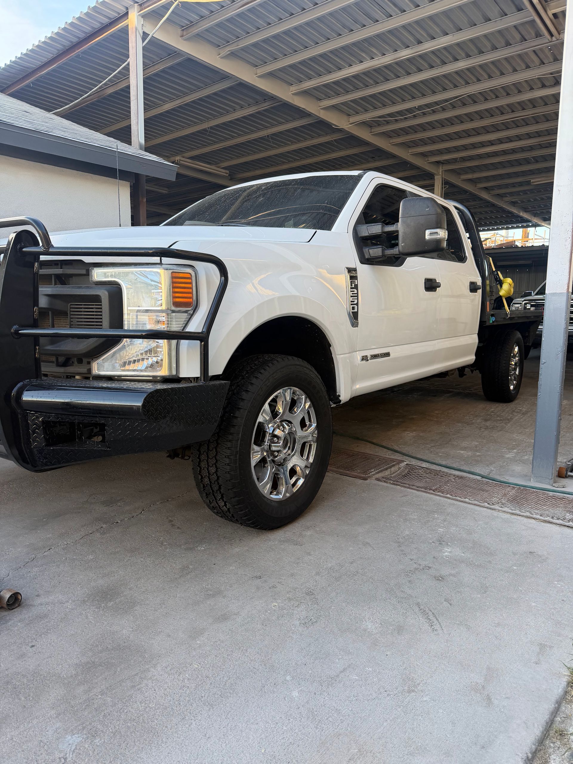 White pickup truck parked under a carport beside a concrete post.