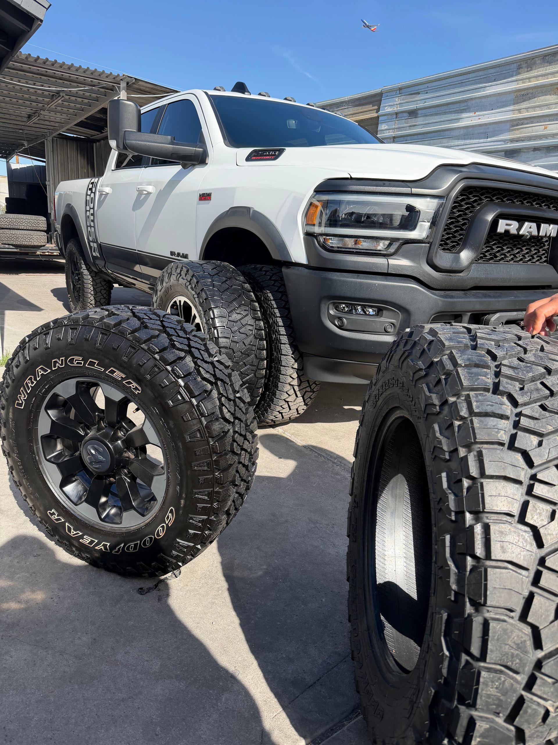 Lifted white pickup truck with oversized off-road tires parked outdoors in bright sun.