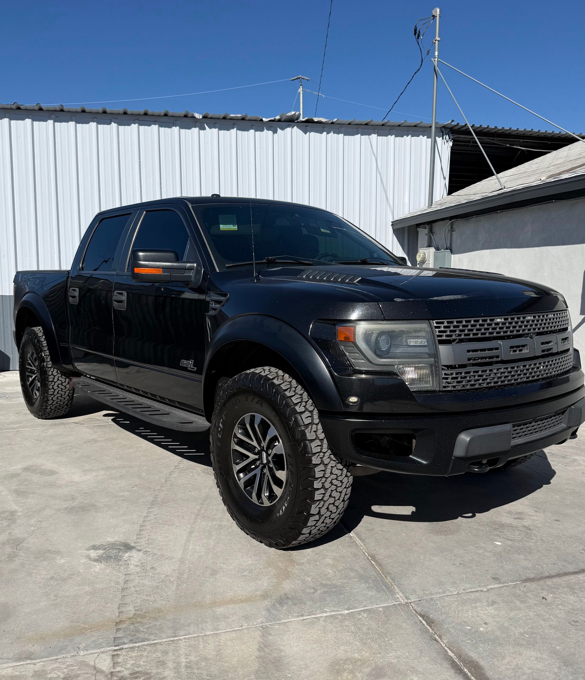 Black pickup truck parked on concrete beside a white metal building on a sunny day