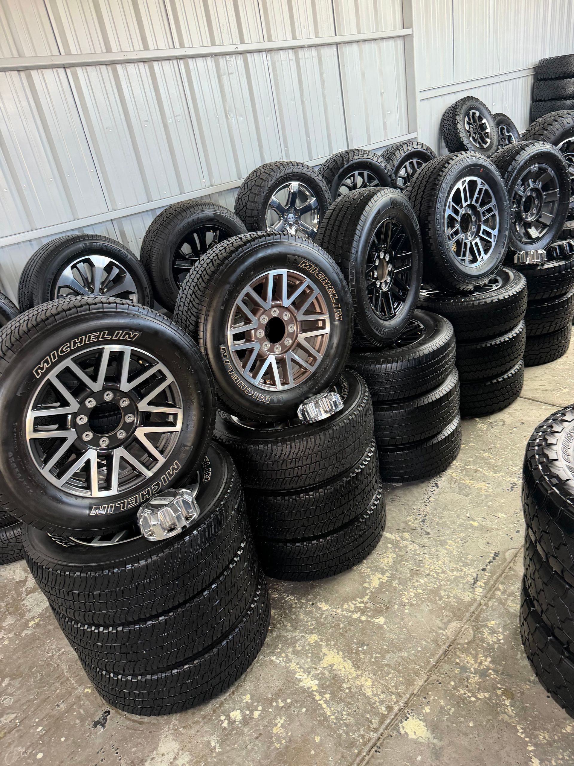 Stacks of car tires with alloy rims lined up against a wall in a garage-like space