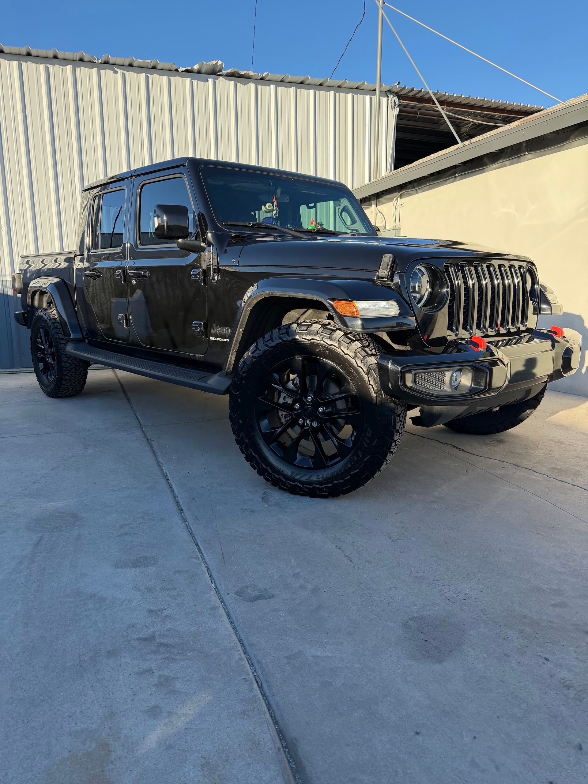 Black Jeep pickup truck parked on concrete beside a corrugated metal building.