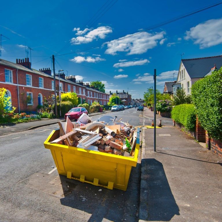 Yellow skip overflowing with debris on a residential street under a blue sky.