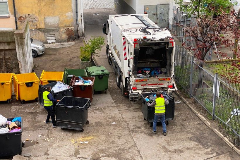 a top down view of waste management workers emptying dumpsters into a truck