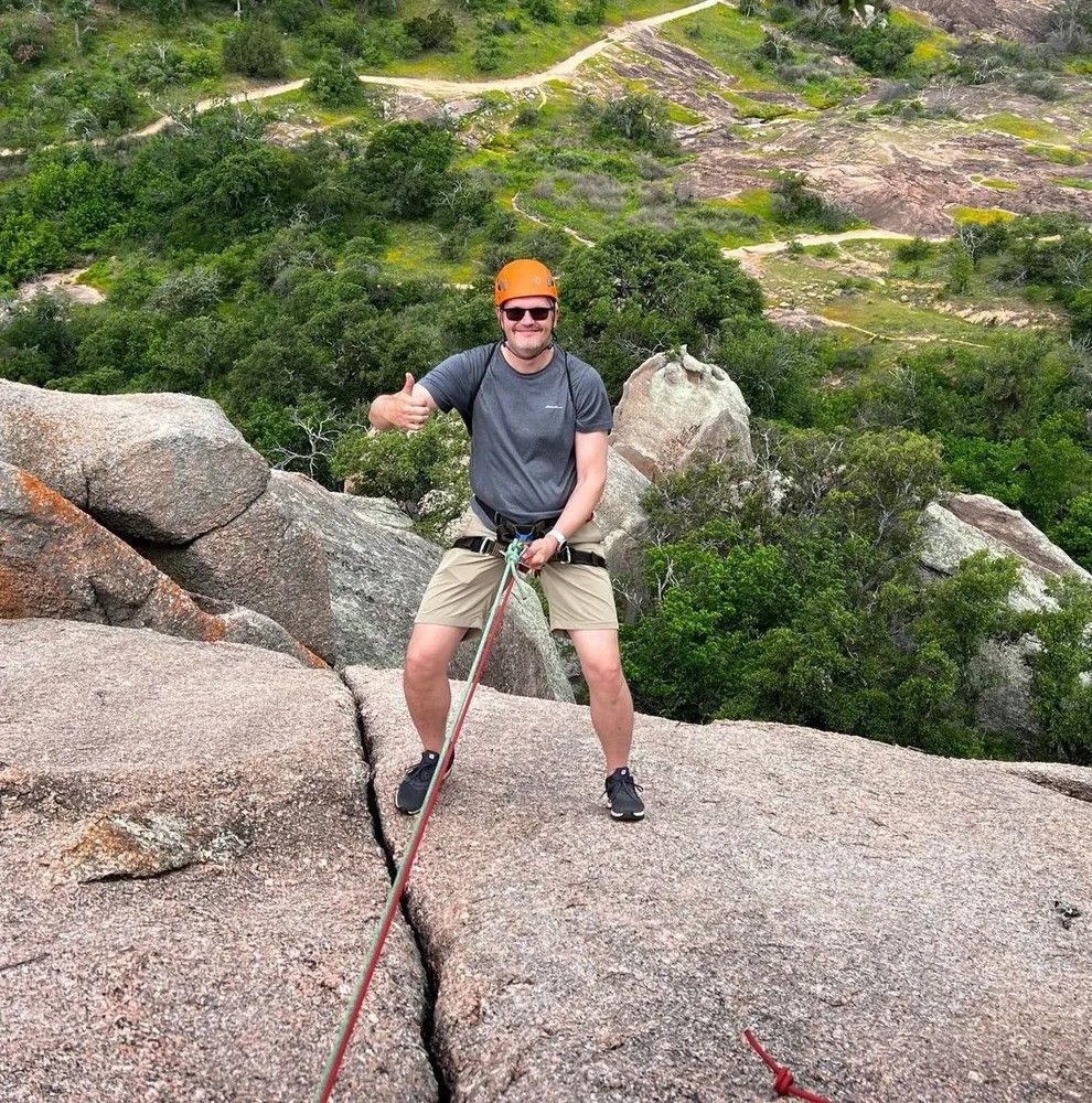A man is standing on top of a rock holding a rope and giving a thumbs up