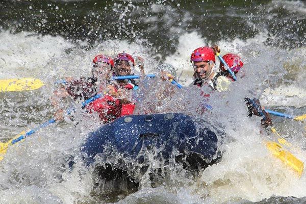 Whitewater rafters in red helmets splash through rapids in a yellow raft