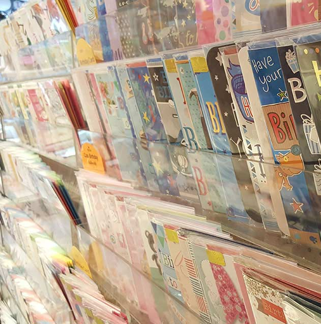 A row of greeting cards are lined up on a shelf in a store.