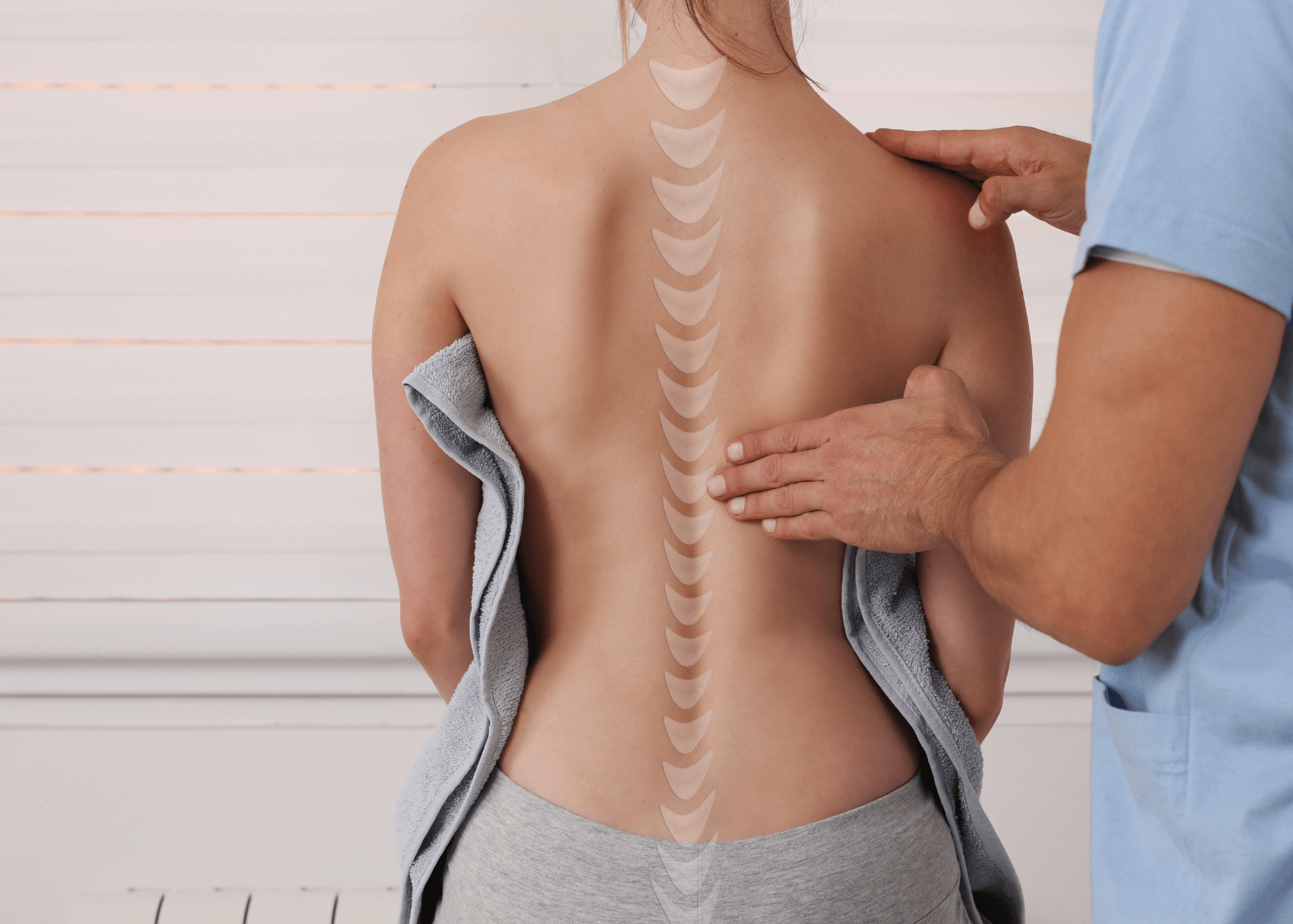 Chiropractor checking a woman’s spine as she stands with a towel in a clinic.