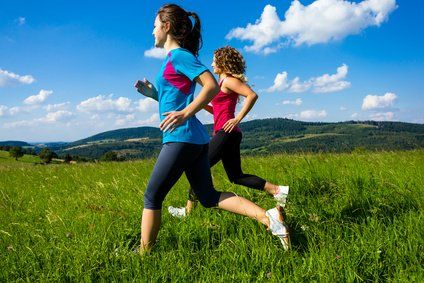 Two women are running in a grassy field.