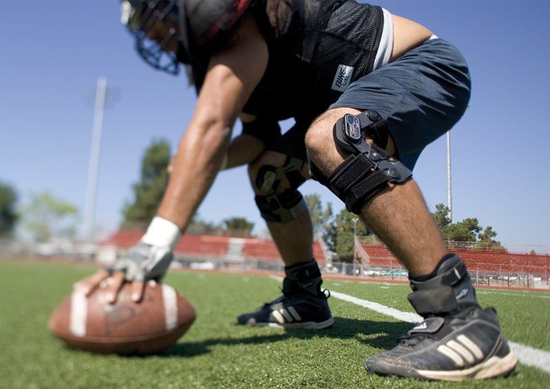 Football player in black crouches at the line of scrimmage on a sunny field