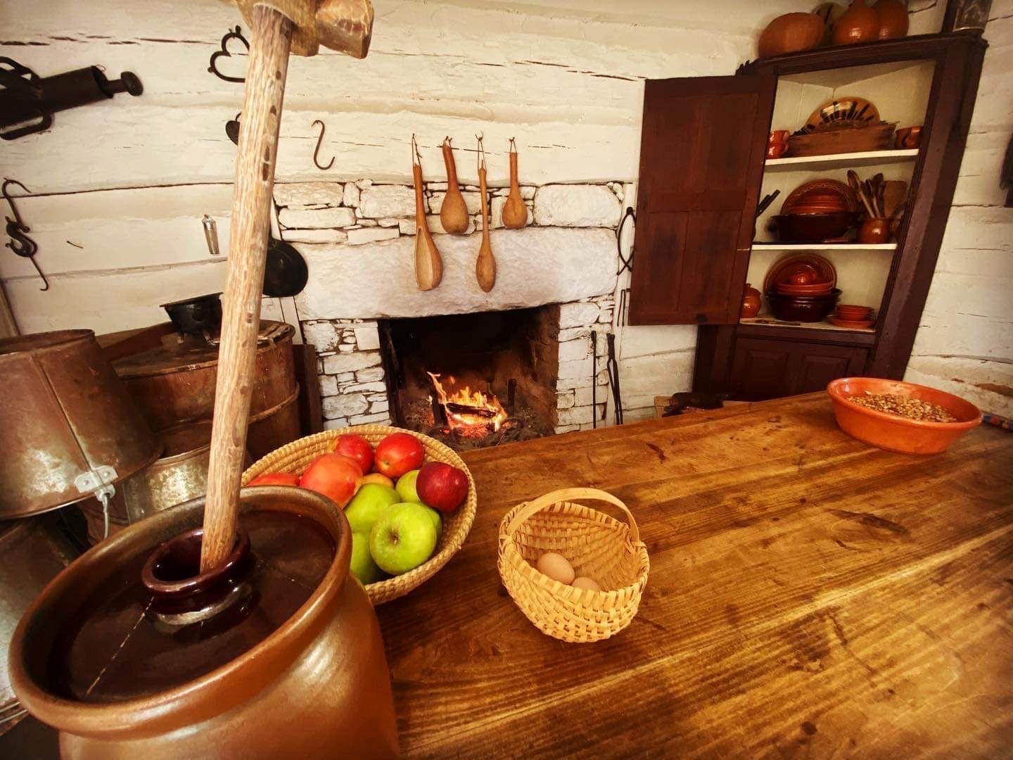 A wooden table with a bowl of fruit and a bowl of eggs in front of a fireplace.