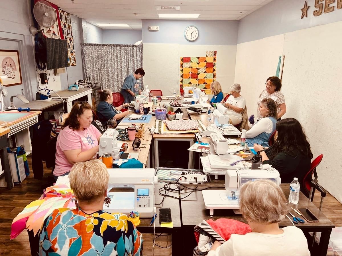 A group of people are sitting at tables in a room using sewing machines.