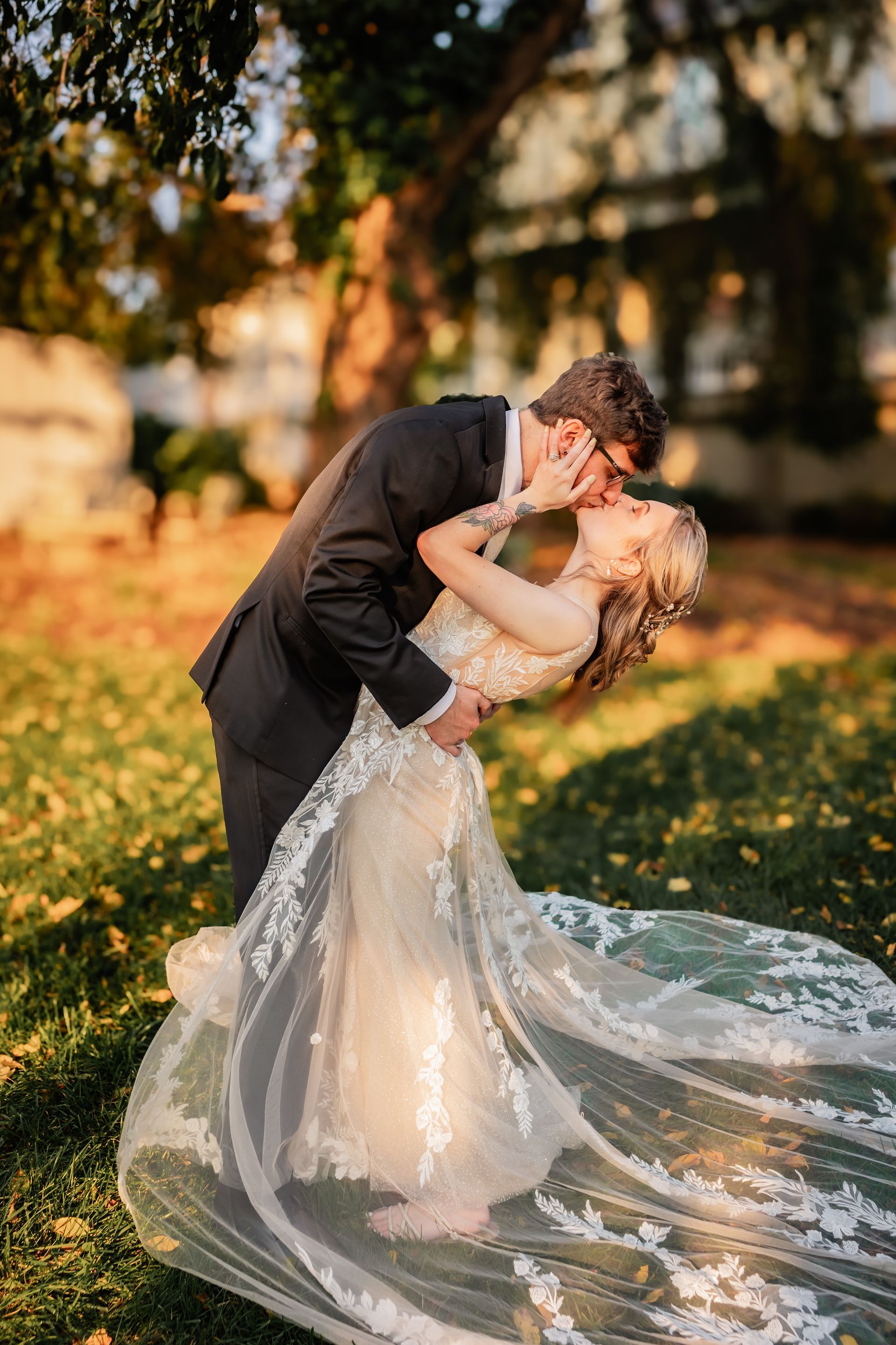 A bride and groom are kissing in a field . the bride is wearing a long veil.