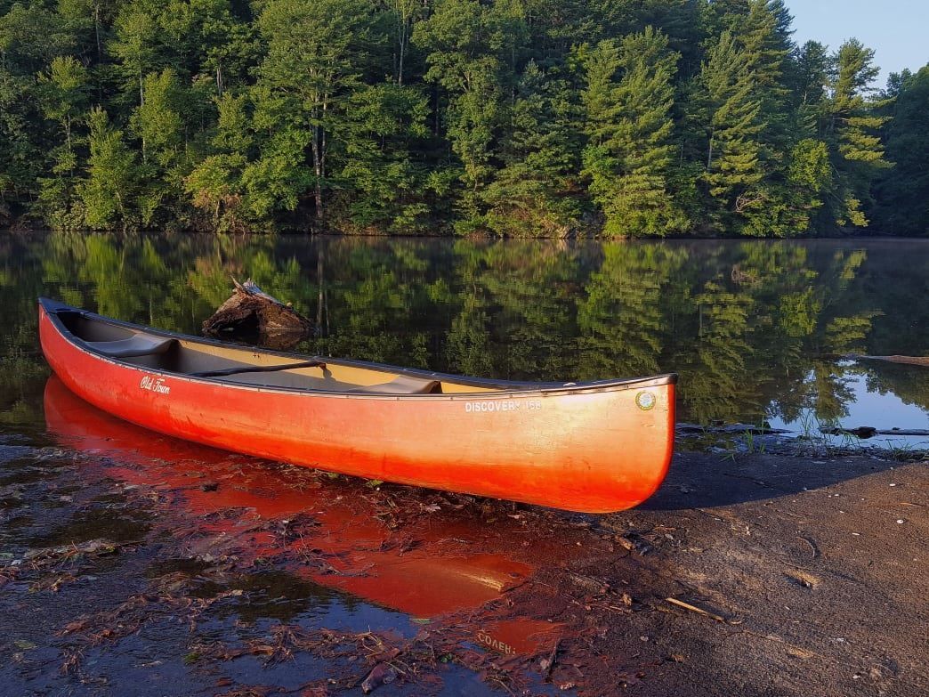 A red canoe is sitting on the shore of a lake.