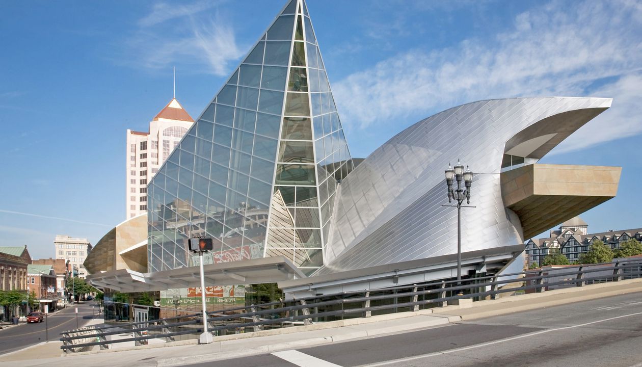 A large building with a pyramid shaped roof is sitting on the side of a city street.