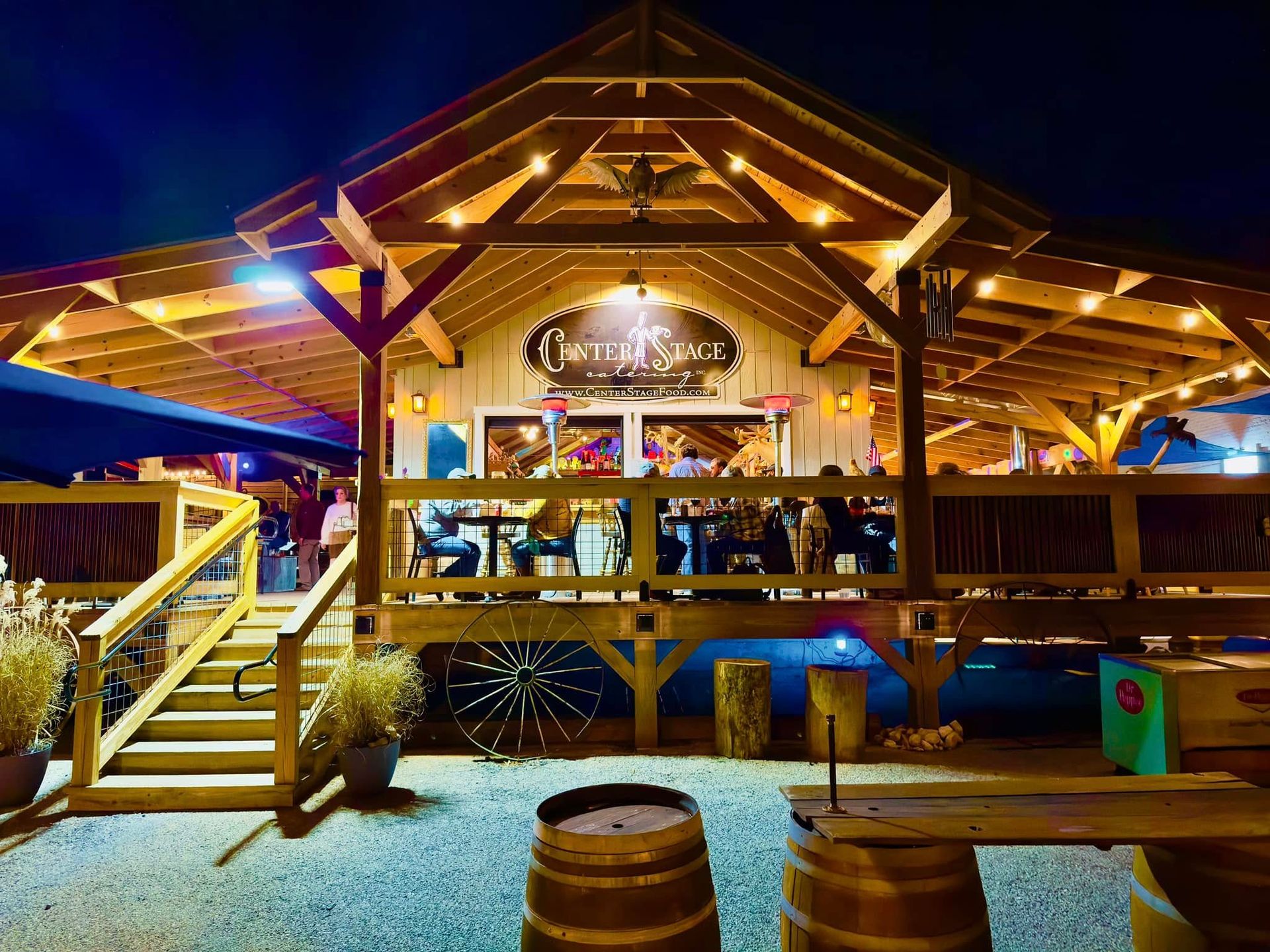 A restaurant with a wooden deck and barrels in front of it at night.