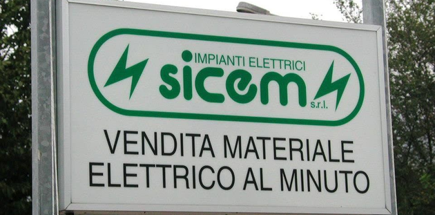 Insegna del negozio di materiale elettrico Sicom, con logo verde e testo in italiano su sfondo bianco.