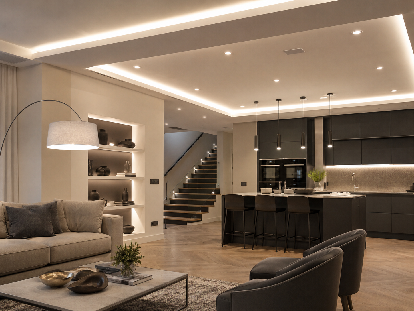 Soggiorno e cucina moderni a pianta aperta con arredamento neutro, illuminazione a incasso, divano grigio e scala.
