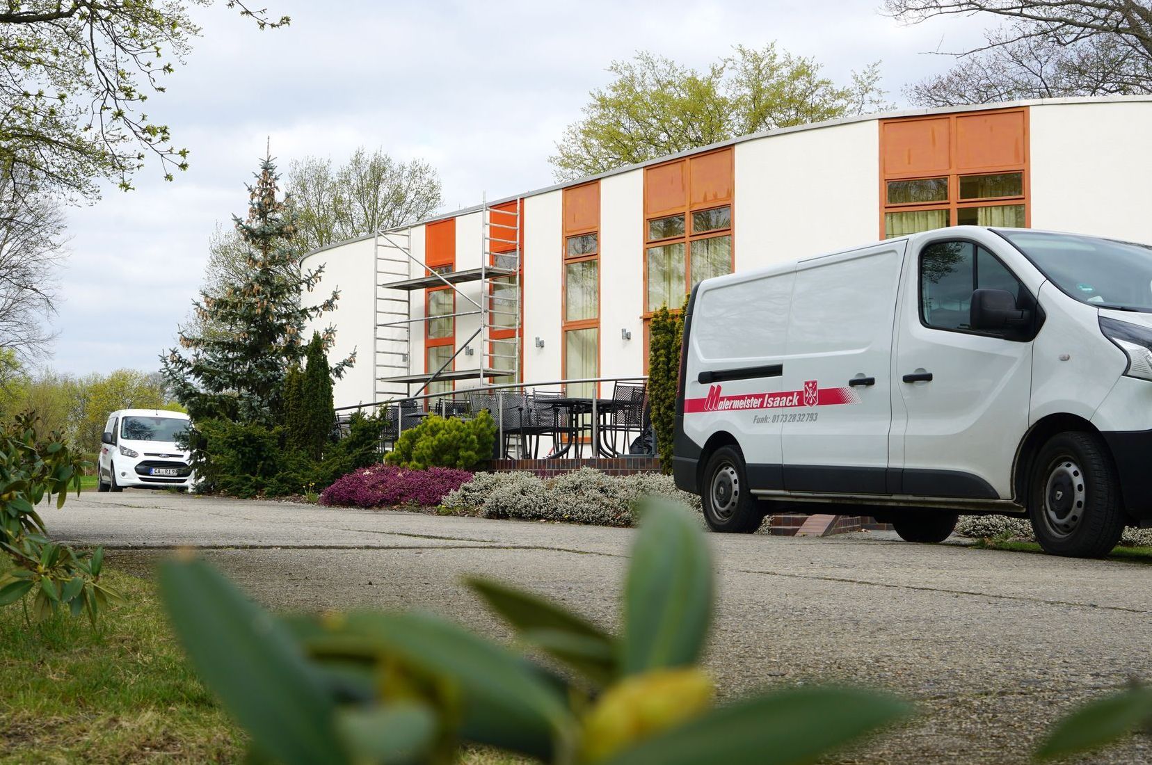 Firmenfahrzeuge vor Gebäude, bei dem die Fenster gestrichen werden