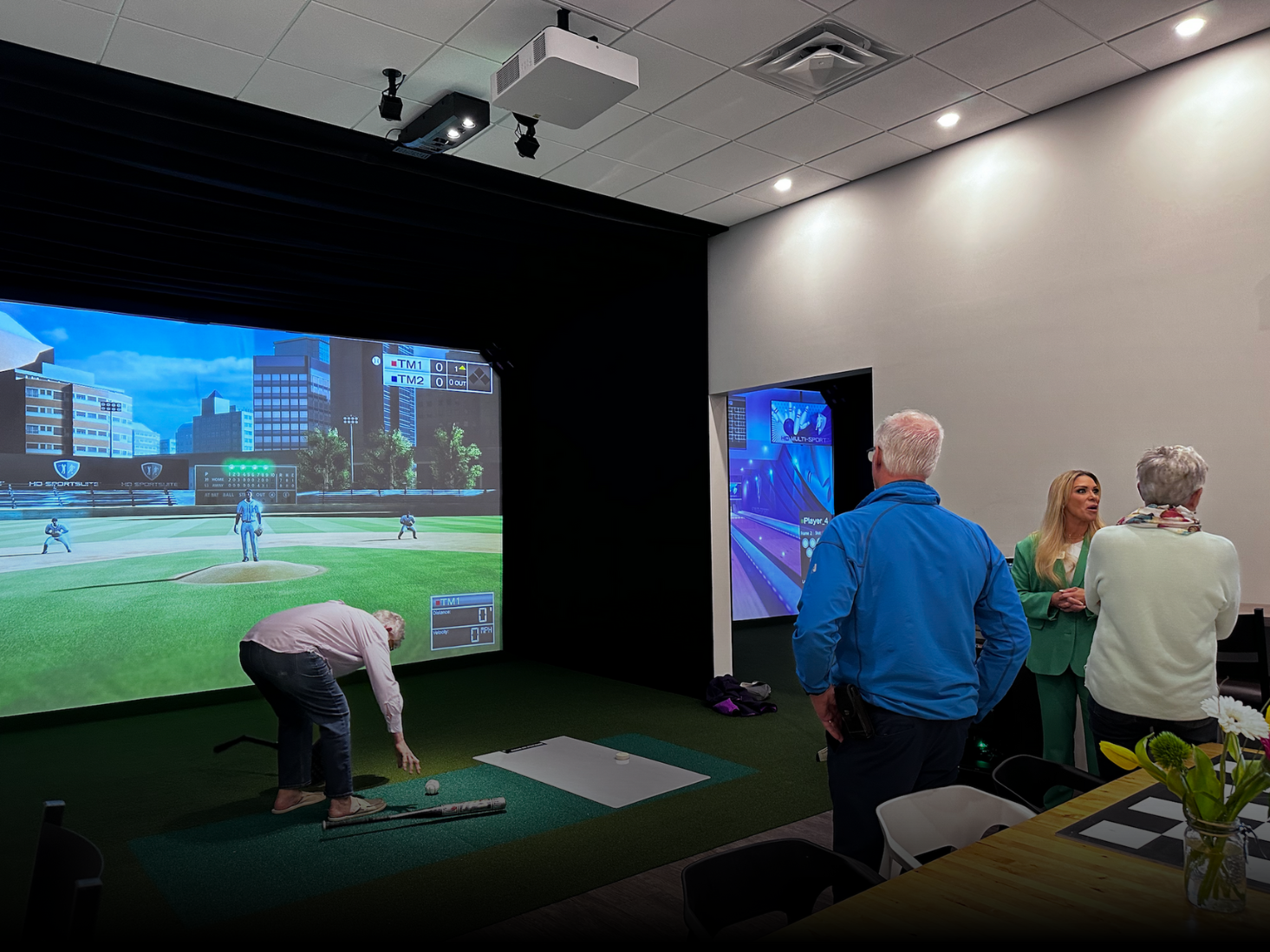 A group of people are watching a baseball game on a large screen.
