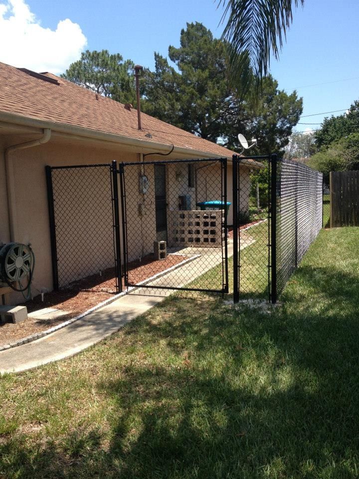 Backyard patio with chain-link fence panels beside a house and grassy lawn.